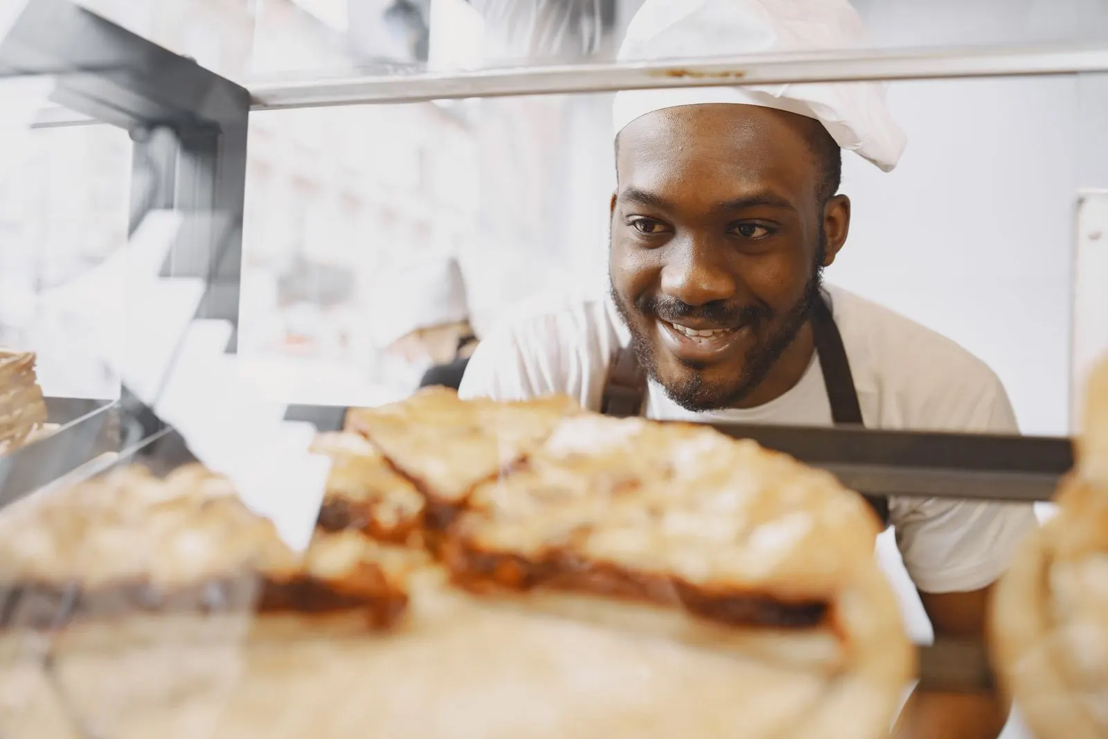 A smiling baker looking through a pastry display case