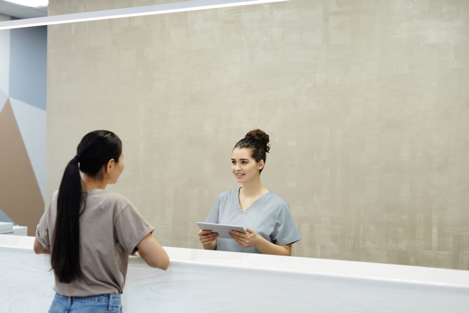 A receptionist with a tablet greeting a visitor at a clinic front desk